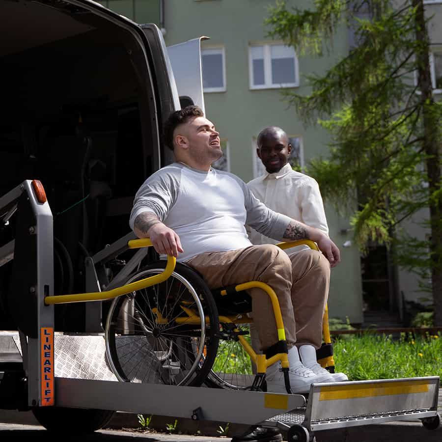 A support worker assisting a wheelchair user from an accessible vehicle